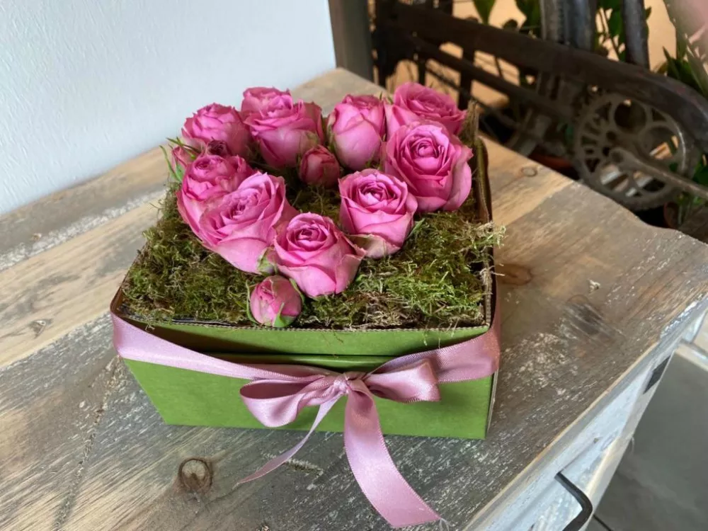 Eine grÃ¼ne Schachtel mit rosa Rosen auf einem Tisch
